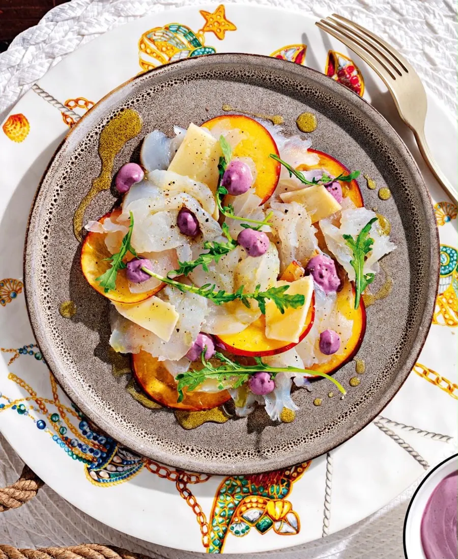 Carpaccio di pesce crudo con pesca e fiori, su piatto di ceramica